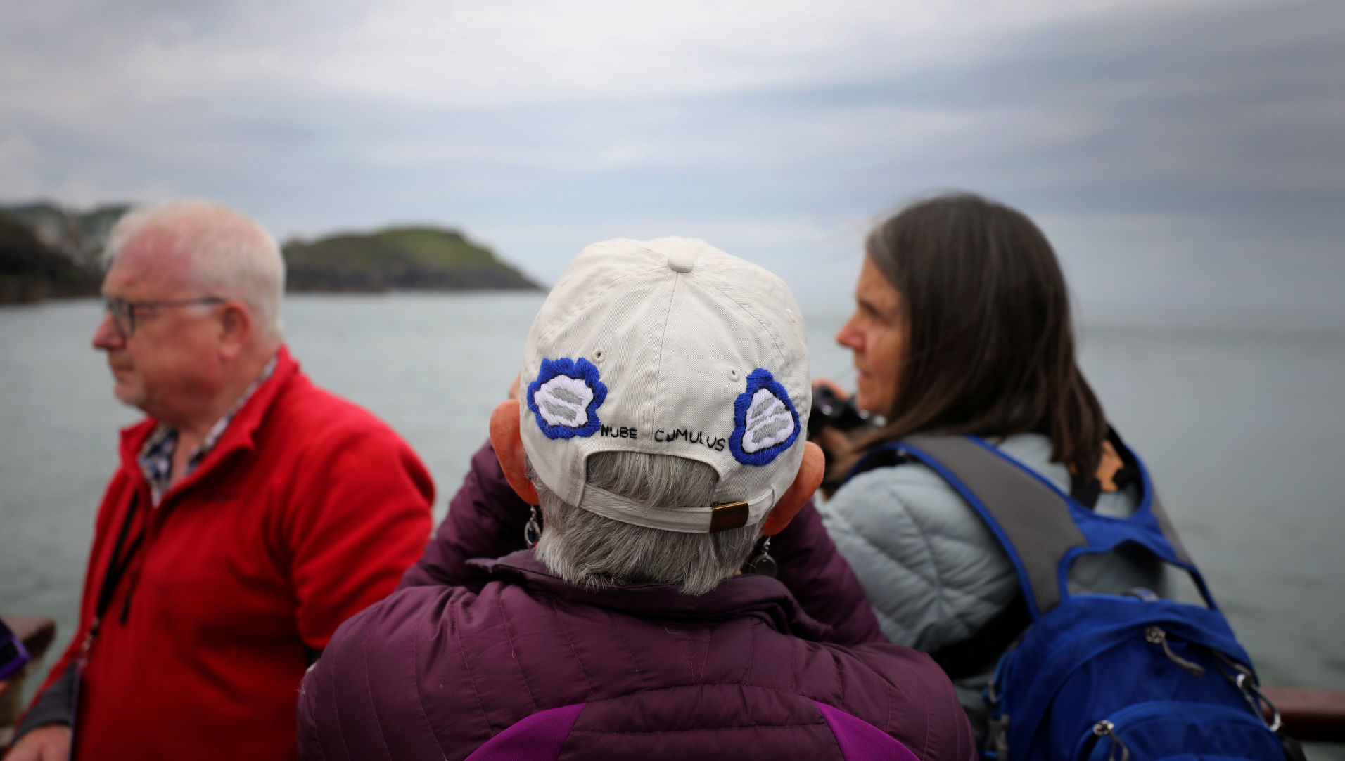 A member of the Cloud Appreciation Society looks through binoculars as she wears a cloud themed cap during the ride on the MS Oldenburg ferry to Lundy